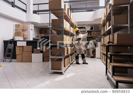 Shipping company worker standing in warehouse aisle near cardboard boxes shelf, using digital tablet and searching customer parcel. Delivery service storage employee looking at packages on metal racks Shipping company worker standing in warehouse aisle near cardboard boxes shelf, using digital tablet and searching customer parcel. Delivery service storage employee looking at packages on metal racks 98959833