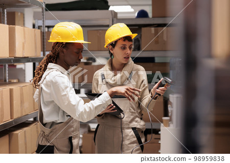 Diverse woman storehouse managers scanning parcels for stock monitoring. Warehouse workers using barcode scanner device for freight inventory in shipping company software Diverse woman storehouse managers scanning parcels for stock monitoring. Warehouse workers using barcode scanner device for freight inventory in shipping company software 98959838