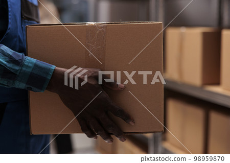 African american warehouse worker hands taking parcel from shelf. Shipping company employee working in storehouse, holding heavy cardboard box with adhesive tape close up 98959870