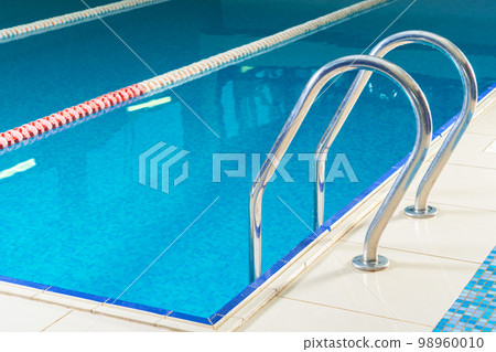 Empty indoor swimming pool with railing and steps in water Empty indoor swimming pool with railing and steps in water 98960010