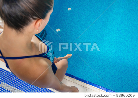 Young woman touching water with foot in indoor swimming pool 98960209