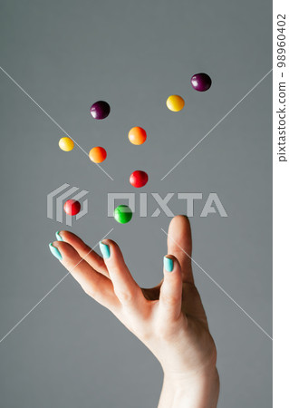 Female hand throwing bright multi-colored round candies into air. Levitating candy, copy space. Vertical Female hand throwing bright multi-colored round candies into air. Levitating candy, copy space. Vertical 98960402