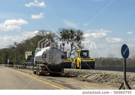 Highway intercity new road construction site with many heavy machinery steamroller, water tanker truck and paver tractor. Paving motorway road street works. Urban infrastructure development industry 98960795