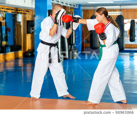Young woman practicing boxing punches in pair with instructor Young woman practicing boxing punches in pair with instructor 98963866