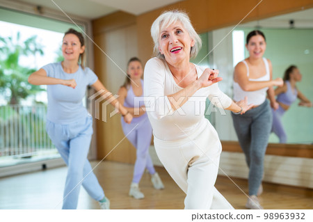 Mature female coach dancing and practicing new movements with group of young women in gym. Dance and wellbeing concept 98963932