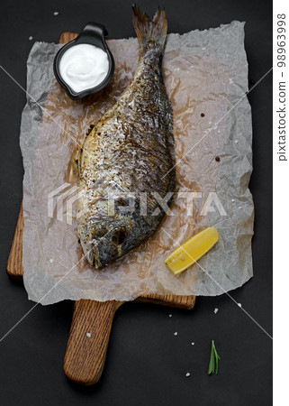 Roasted sea bream fish with herbs on a cutting board. Black background. Top view 98963998