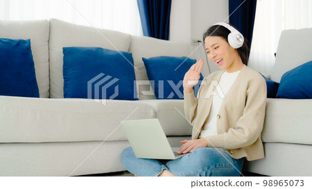 Young asian woman wearing headset while working on computer laptop at house 98965073