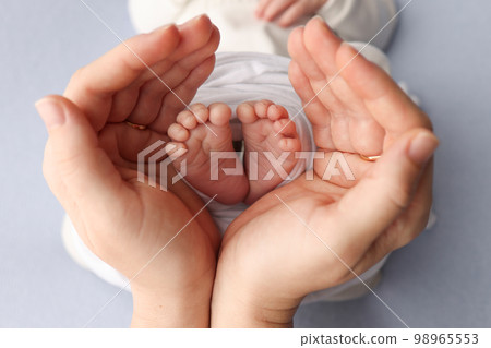 Small feet of a newborn in the hands of parents. Loving palms of the hands of mother. Conceptual image of fatherhood. Close-up, selective focus. Professional photography a white background. 98965553