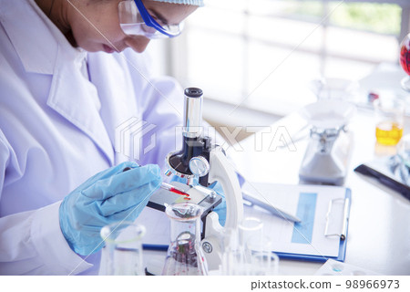 Woman scientist hand write note information in medical lab look at science microscope medical test, research biology chemistry. Asian Females technician laboratory analyzing blood test pharmaceutical Woman scientist hand write note information in medical lab look at science microscope medical test, research biology chemistry. Asian Females technician laboratory analyzing blood test pharmaceutical 98966973