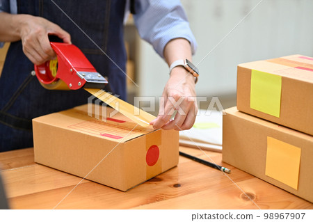 A female e-commerce business startup or worker packing her shipping box in stock room. A female e-commerce business startup or worker packing her shipping box in stock room. 98967907