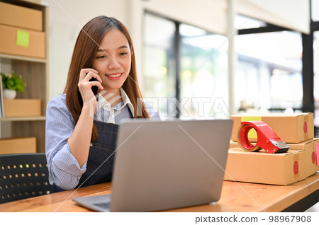 Asian female store owner looking at a laptop screen while on the phone with her supplier Asian female store owner looking at a laptop screen while on the phone with her supplier 98967908