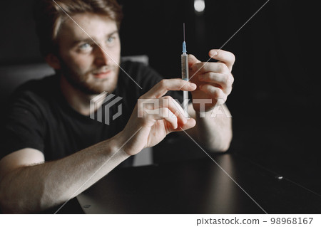 Drug addiction concept. Young sick drug addict man. He is sitting alone and about to take a dose. Drug addiction concept. Young sick drug addict man. He is sitting alone and about to take a dose. 98968167