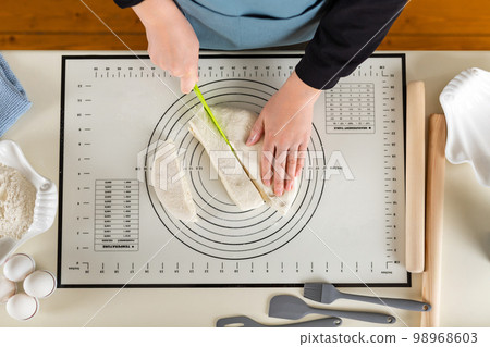 Cutting dough on a silicone baking mat with a special plastic knife, top view 98968603