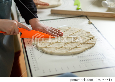 Side view of cutting dough with a plastic knife on a silicone baking mat 98968613