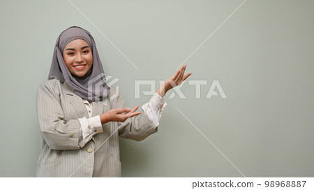 Beautiful Asian Muslim woman standing with open palm over isolated grey background. 98968887
