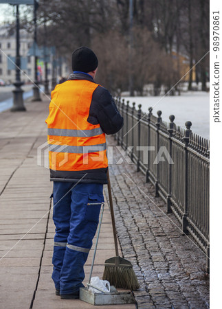 Migrant janitor in bright vest rests while working on the sidewalk. Migrant janitor in bright vest rests while working on the sidewalk. 98970861
