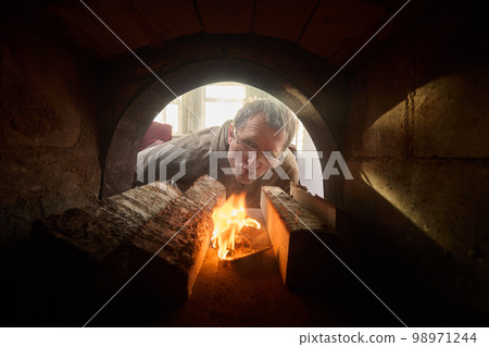 Homeowner makes fire in firebox of wood burning stove to heat home. 98971244