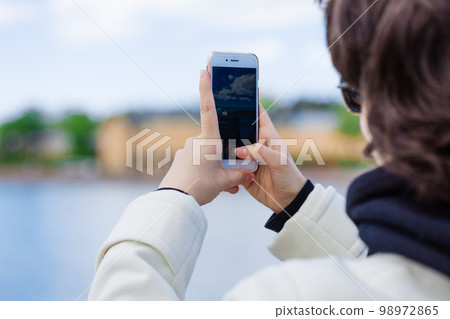 Young woman on vacation using mobile phone to take pictures river and city 98972865