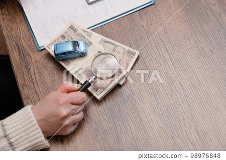 [A housewife carefully examining her car purchase with a magnifying glass] 98976848