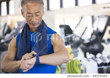 Middle-aged man operating smart watch at fitness gym Middle-aged man operating smart watch at fitness gym 98976889
