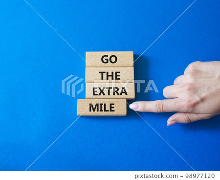 Go the extra mile symbol. Wooden blocks with words Go the extra mile. Businessman hand. Beautiful blue background. Business and Go the extra mile concept. Copy space. 98977120