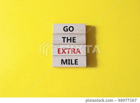 Go the extra mile symbol. Wooden blocks with words Go the extra mile. Beautiful yellow background. Business and Go the extra mile concept. Copy space. 98977167