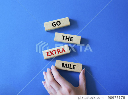 Go the extra mile symbol. Wooden blocks with words Go the extra mile. Businessman hand. Beautiful blue background. Business and Go the extra mile concept. Copy space. Go the extra mile symbol. Wooden blocks with words Go the extra mile. Businessman hand. Beautiful blue background. Business and Go the extra mile concept. Copy space. 98977176