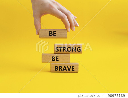 Be strong be brave symbol. Concept words Be strong be brave on wooden blocks. Beautiful yellow background. Businessman hand. Business concept. Copy space. 98977189