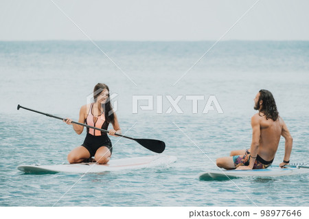 Sea woman and man on sup. Silhouette of happy young woman and man, surfing on SUP board, confident paddling through water surface. Idyllic sunset. Active lifestyle at sea or river. 98977646