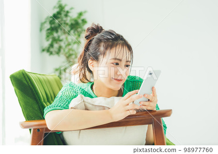 一個女人躺在沙發上，看著她的智能手機 98977760