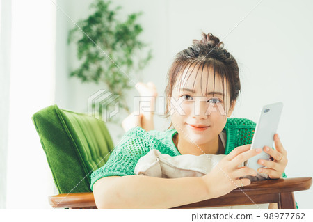 一個女人躺在沙發上,看著她的智能手機 一個女人躺在沙發上,看著她的智能手機 98977762