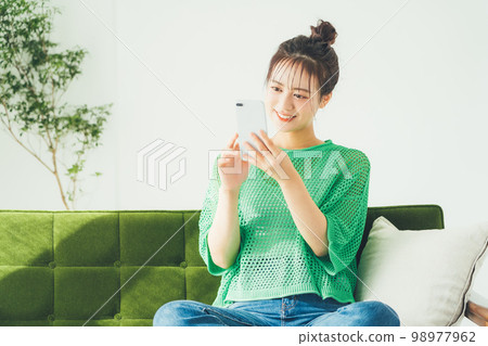 Woman sitting on a sofa and looking at a smartphone 98977962