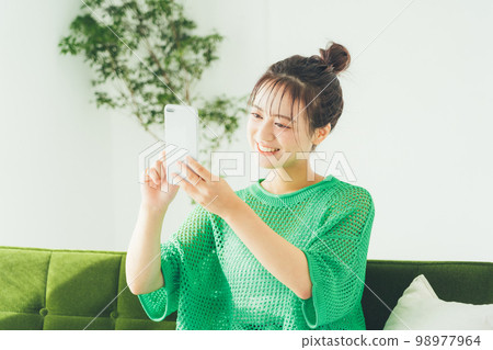 Woman sitting on a sofa and looking at a smartphone Woman sitting on a sofa and looking at a smartphone 98977964