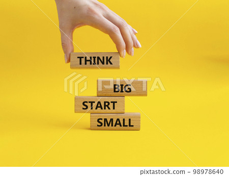 Think big start small symbol. Concept words Think big start small on wooden blocks. Beautiful yellow background. Businessman hand. Business and Think big start small concept. Copy space Think big start small symbol. Concept words Think big start small on wooden blocks. Beautiful yellow background. Businessman hand. Business and Think big start small concept. Copy space 98978640