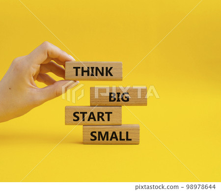 Think big start small symbol. Concept words Think big start small on wooden blocks. Beautiful yellow background. Businessman hand. Business and Think big start small concept. Copy space Think big start small symbol. Concept words Think big start small on wooden blocks. Beautiful yellow background. Businessman hand. Business and Think big start small concept. Copy space 98978644