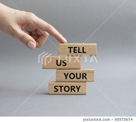 Tell us your story symbol. Concept words Tell us your story on wooden blocks. Beautiful grey background. Businessman hand. Business and Tell us your story concept. Copy space. 98978654