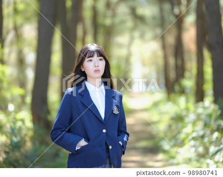 Female high school student looking into the distance on the road where the sun shines through the foliage Female high school student looking into the distance on the road where the sun shines through the foliage 98980741