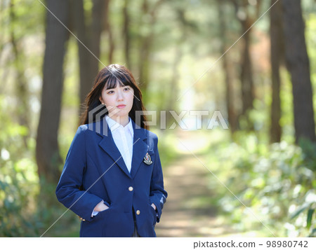 Female high school student looking into the distance on the road where the sun shines through the foliage Female high school student looking into the distance on the road where the sun shines through the foliage 98980742