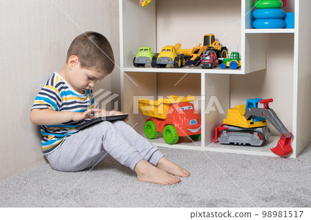 A little boy 3-4 years old looks into the screen of the tablet. Cartoons for children, screen time, children's dependence on the computer and phone A little boy 3-4 years old looks into the screen of the tablet. Cartoons for children, screen time, children's dependence on the computer and phone 98981517