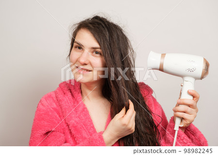 A beautiful happy woman dries her wet hair with a hair dryer and smiles 98982245