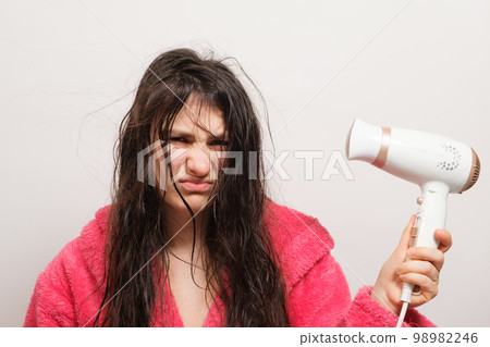 A brunette woman with matted hair dries it with a hair dryer. Hair care, overdried hair A brunette woman with matted hair dries it with a hair dryer. Hair care, overdried hair 98982246