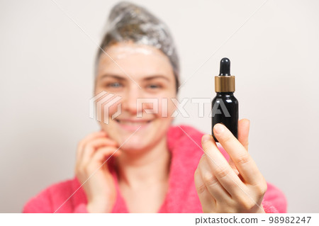 A woman with a film on her head holds a bottle of natural hair oil. Hair care at home, preparations for hair growth 98982247