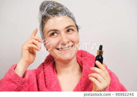 A woman with a film on her head holds a bottle of natural hair oil. Hair care at home, preparations for hair growth 98982248