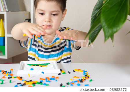 Preschooler child plays with mosaics, small objects for toddlers, careful use under adult supervision. 98982272