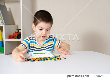 A boy of 4 years old plays with a mosaic, collects a picture from small plastic parts. Development of fine motor skills in children A boy of 4 years old plays with a mosaic, collects a picture from small plastic parts. Development of fine motor skills in children 98982300