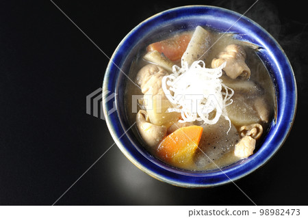 A bird's-eye view of a hot pork offal stew with carrots, konjac, burdock, and radish on a black background A bird's-eye view of a hot pork offal stew with carrots, konjac, burdock, and radish on a black background 98982473