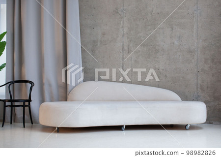 Modern interior with a white velor sofa against a concrete wall. Modern interior with a white velor sofa against a concrete wall. 98982826