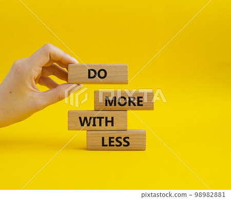 Do more with less symbol. Concept words Do more with less on wooden blocks. Beautiful yellow background. Businessman hand. Business and Do more with less concept. Copy space. Do more with less symbol. Concept words Do more with less on wooden blocks. Beautiful yellow background. Businessman hand. Business and Do more with less concept. Copy space. 98982881