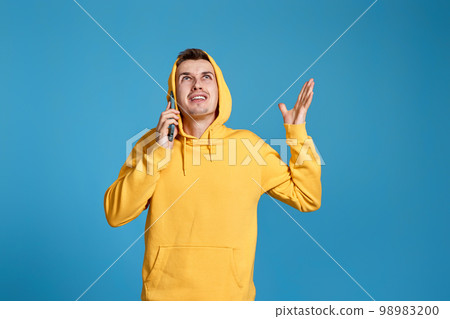 angry man in yellow sweatshirt holding mobile phone angry man in yellow sweatshirt holding mobile phone 98983200