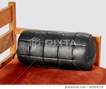 Black leather bolster cushion lying on wooden sofa 98984216